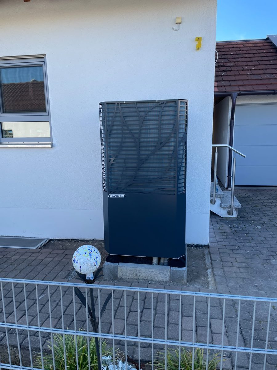 Wärmepumpe auf einem Betonsockel neben der Einfahrt eines Hauses