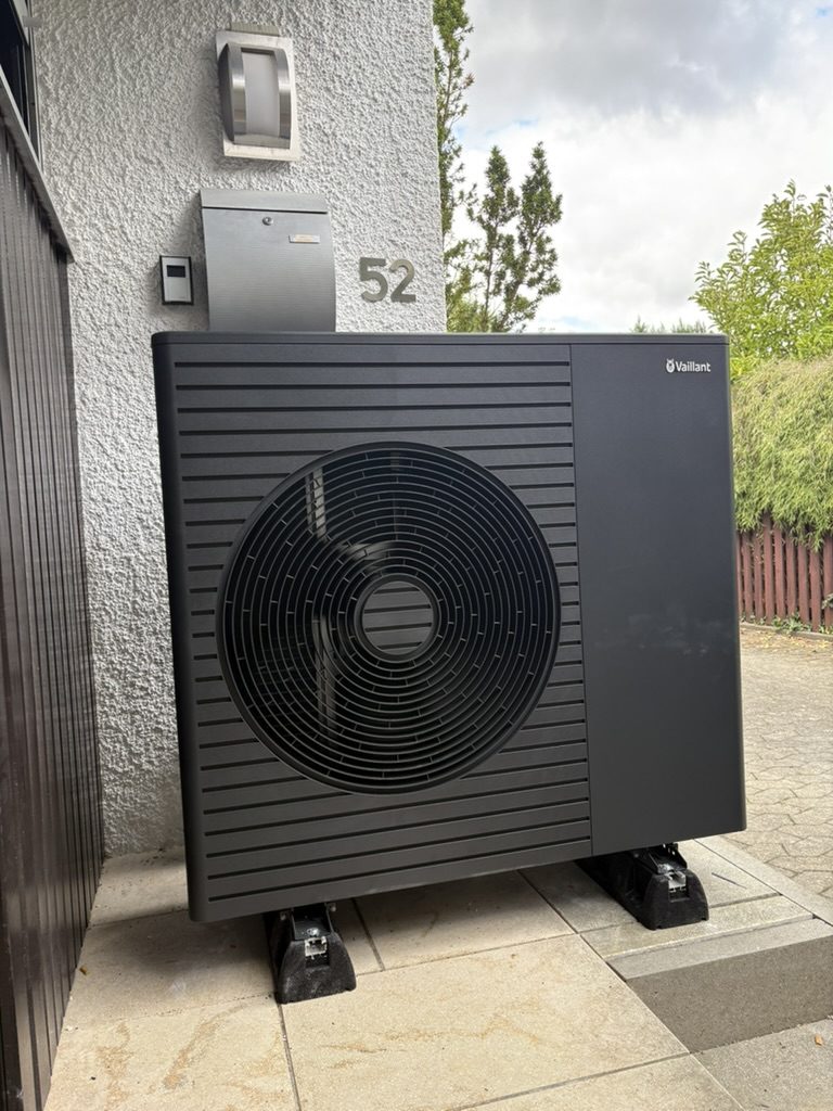 Wärmepumpe direkt neben der weißen Außenwand eines Wohnhauses